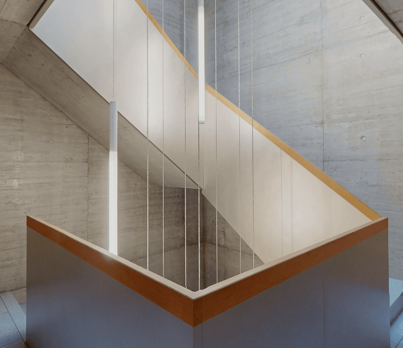 Treppenhaus in Sichtbeton mit Holzhandlauf von unten fotografiert