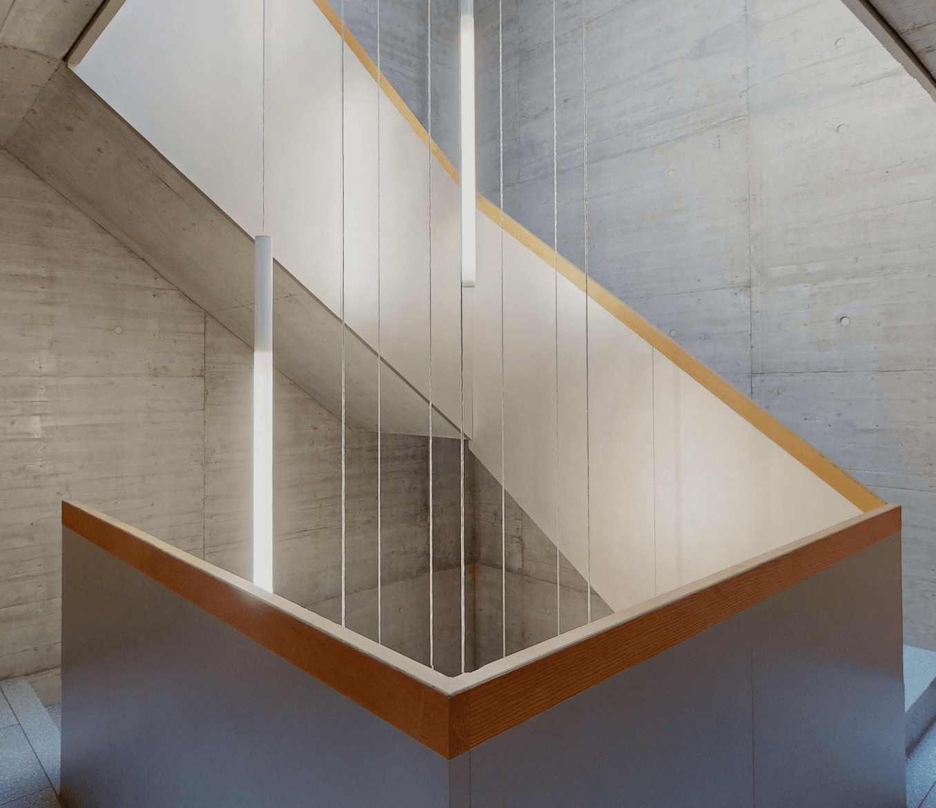 Treppenhaus in Sichtbeton mit Holzhandlauf von unten fotografiert